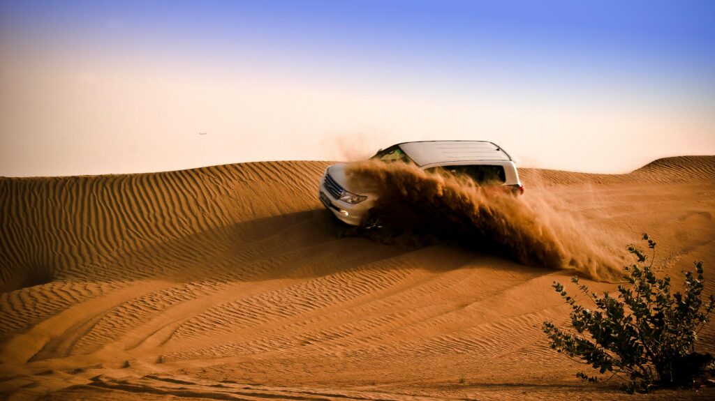 White SUV driving through the sandy dunes of Dubai desert, illustrating thrilling off-road adventure.